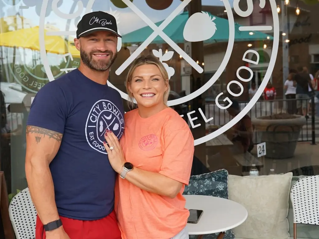 Two City Bowls team members in branded shirts outside a storefront window bearing the Eat Good Feel Good logo